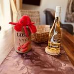 Auf Tisch steht eine Flasche Weißwein und ein roter Plüschkrabbe auf einem Keramikbecher.