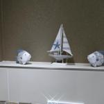 On a shelf are two fish figurines and a sailboat model.