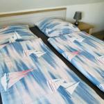 Two beds with sailboat-patterned bedding and a nightstand with a lamp.