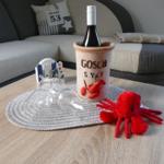 Table with wine cooler, glasses, and red plush toy in front of sofa.