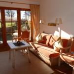 Wohnzimmer mit Sofa, zwei Stühlen und Tisch. Durchgangstür mit Blick auf Garten.