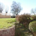 Steinstufen führen durch einen Garten mit Gras, Sträuchern und Bäumen.