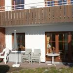 Terrasse mit Tisch, Stühlen und Sonnenschirm. Holzgeländer und Fenster sichtbar.