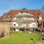 Haus mit mehreren Balkonen und rotem Dach, umgeben von Grünfläche und Steinen.