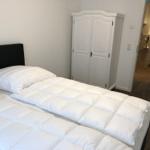 Schlafzimmer mit Bett, Kleiderschrank und Blick in die Badewanne.