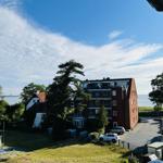 Red building with balconies, surrounded by green areas and a lake.