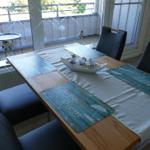 Dining table with four chairs and blue placemats near window with balcony view.