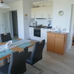 Dining room with table, chairs, and kitchen area. Bedroom with bed visible.