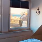 A bed with blue bedding in front of a window with sea view and a white anchor on the wall.