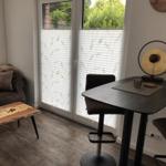 Ein Raum mit Sofa, Tisch und Stühlen vor einer Glastür mit Jalousien.