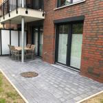 Terrasse mit Tisch und Stühlen neben rotem Backsteinhaus mit Glasfronten.