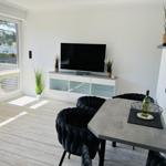 Living and dining area with TV, table and chairs. Windows to the terrace.