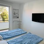 Room with two beds, TV, and balcony view of green areas.