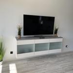 Flat-screen TV on modern cabinet with glass fronts and plants.