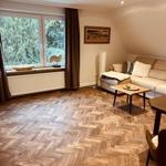 Wohnzimmer mit Holzboden, Sofa und Fenster mit Blick auf Bäume