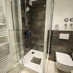 Dusche mit Glaswand, Toilette und Handtuchheizung in moderner Badezimmerausstattung.