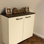 Weißer Schrank mit dunkler Arbeitsplatte und Seil-Schriftzug. Hintergrund Wand und Holzboden.