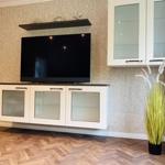 Wohnzimmer mit Fernseher, Schrank und Pflanze auf Holzboden.