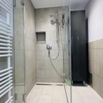 Dusche mit Glaswand, Duschbrause und Heizkörper an der Wand