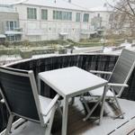 Balkon mit Tisch und zwei Stühlen, bedeckt mit Schnee. Blick auf Wohngebäude und Garten.
