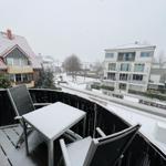 Balkon mit Tisch und Stühlen im Schnee. Blick auf Wohnhäuser und verschneite Straße.