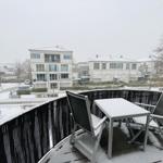 Terrasse mit Tisch und zwei Stühlen, bedeckt mit Schnee, Blick auf Wohnhäuser.