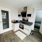 Küche mit Arbeitsplatte, Herd und Dunstabzug. Tür zum Balkon und Schlafzimmer sichtbar.