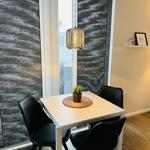 Ein Essbereich mit weißem Tisch, drei schwarzen Stühlen und einer Pflanze auf dem Tisch.