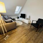 Wohnzimmer mit Sofa, Sessel, Fernseher und Holzboden