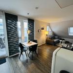 Wohnbereich mit Essbereich, Sofa und Balkon. Holzboden und große Fenster.