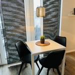 Essbereich mit weißem Tisch, drei schwarzen Stühlen und Pflanze. Hängelampe und Fenster mit Jalousie.