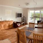 Living and dining area with wooden furniture and large window. Kitchen on the left.