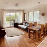 Living and dining area with wooden floor, sofa, dining table, and view to terrace.
