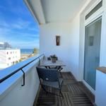 Balkon mit Tisch, Stühlen und Meerblick. Holzdecke und Fenster mit Jalousien.