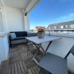 Terrasse mit Tisch, Stühlen und Pflanze. Blick auf Dächer und Himmel.