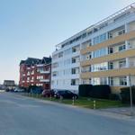 Wohnhaus mit Balkonen und gepflegtem Grünstreifen entlang der Straße.