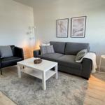 Wohnzimmer mit grauem Sofa, schwarzer Sitzgelegenheit und weißem Couchtisch.