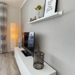 TV-Schrank mit Bild, Blumen und Korb. Hintergrund: Lampe und Vorhang.