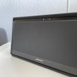 Bose-Lautsprecher auf runder Tischplatte mit grauer Sitzgelegenheit im Hintergrund.