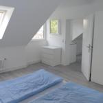 Schlafzimmer mit Dachschrägen, Fenster und weißem Schrank.