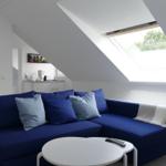 Ein Wohnzimmer mit blauem Sofa, runder Tisch und Dachfenster.