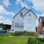 White house with balcony and garden. Background: other houses and blue sky.