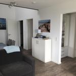 Living room with sofa, dining table, and TV. White walls and wooden floor.