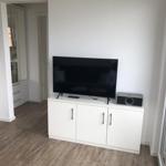TV on white cabinet, speaker beside, window nearby