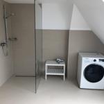 Shower with glass partition, washing machine, and small white stool.