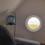 Round window offers view of beach and sea. Next to a gray armchair stands a floor lamp.