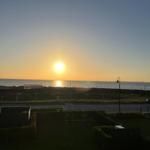 Sunset over the sea with road and green areas in the foreground.