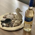 A bottle of white wine next to a dish with shells and a seahorse.