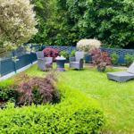 Garten mit Liegestuhl, Sitzgruppe und Pflanzen hinter blauem Zaun.