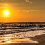 Sonnenuntergang am Strand mit Wellen und einem Schiff im Hintergrund.